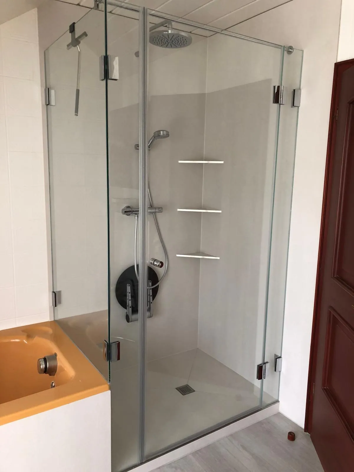 Eckdusche aus Klarglas mit Ablagenischen in der gefliesten Wand, Holzboden davor